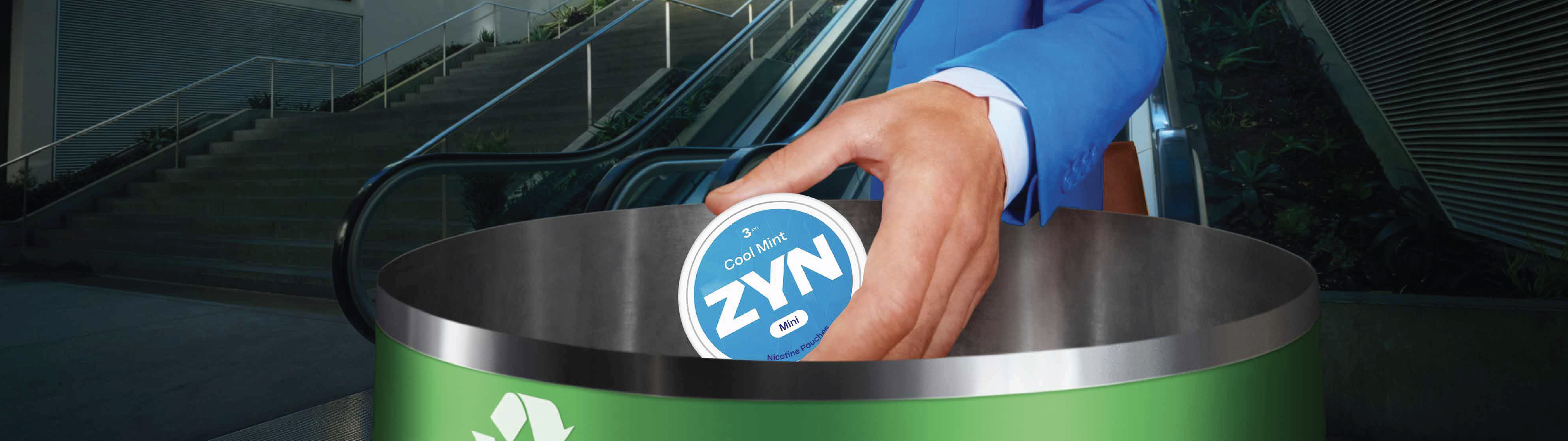 Image of a man in a blue suit placing a ZYN container into a green recycling bin with escalators and stairs behind him.